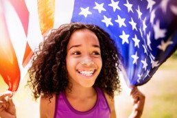 Happy young Afro girl holding an American flag over her head and smiling positively