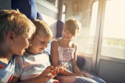 Kids travelling to visit Rome by train. Little girl and two boys are smiling and playing with smartphone. Italy, Tuscany.