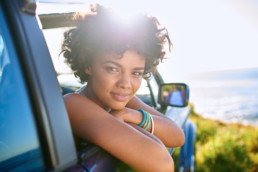 A woman looks at the photographer as she hangs out the car window.