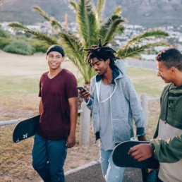 3 friends about to go skateboarding while one looks at his phone.