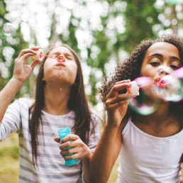 Two tween girls blowing bubbles outdoors.