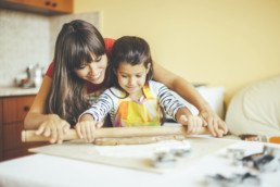 A mother and daughter using a rolling pin to bake something.
